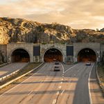 A highway with two tunnel entrances surrounded by rocky terrain and cars driving