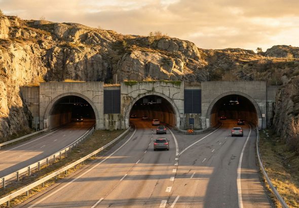 A highway with two tunnel entrances surrounded by rocky terrain and cars driving