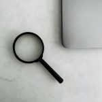 A magnifying glass placed next to a laptop on a white surface