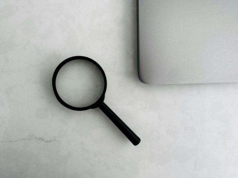 A magnifying glass placed next to a laptop on a white surface