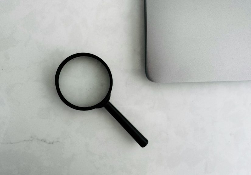 A magnifying glass placed next to a laptop on a white surface